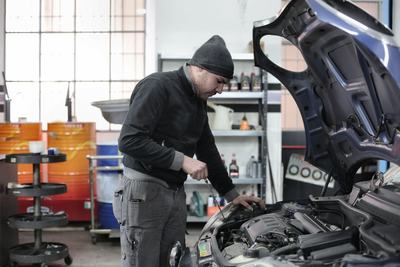 Mechanic leaning over an open hood checking the engine