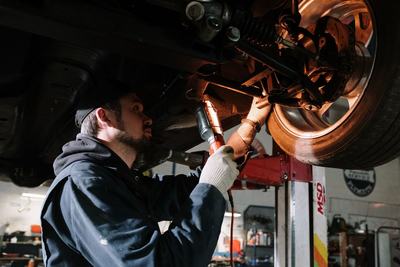 Mechanic working on suspension components under a lifted car with a worklight