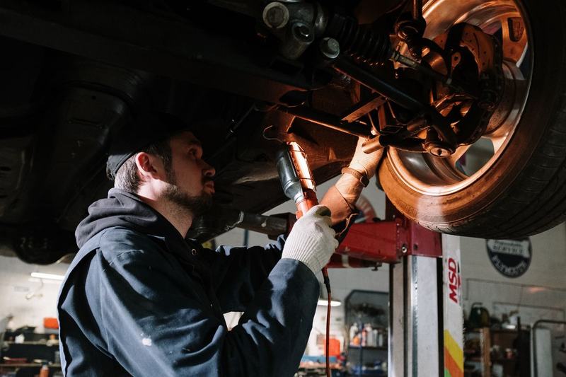 Mechanic working on suspension components under a lifted car with a worklight