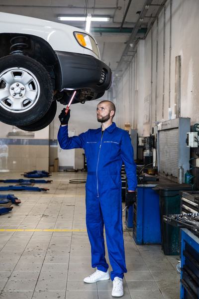 Mechanic shining a worklight on the underside of a lifted truck